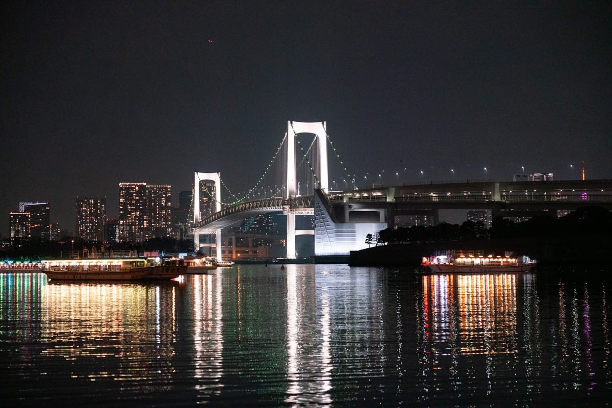 夜晚的彩虹大桥，桥上灯光和对岸高楼倒映在东京湾水面